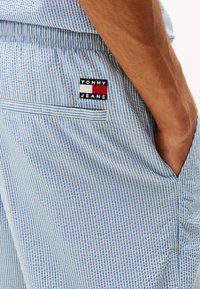 Lys blå og hvite stripete bukser med en baklomme med en "TOMMY JEANS" etikett. Stoffet fremstår teksturert med en avslappet passform.