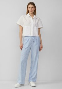 Kort wit shirt met korte mouwen en twee voorzakken, gecombineerd met lichtblauwe gestreepte broeken en witte sneakers. Eenvoudig ontwerp en pasvorm.