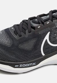 Sort Nike ZoomX løbesko med en tekstureret overdel, grå detaljer, fremtrædende snøresystem og et hvidt swoosh-logo på siden.