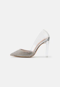 Genomskinlig pumpsko med spetsig tå, dekorerad med silverfärgade rhinestones på en texturerad yta. Genomskinliga sidor och stillettklack.