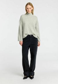 Světle šedý oversized svetr s rolákem, zkombinovaný s jeansy z tmavého denimu s vysokým pasem, které mají široké nohavice a složené manžety. Černé špičaté boty.