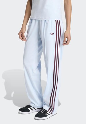 Person wearing light blue track pants with three maroon stripes and Adidas logo, paired with black and white sneakers.