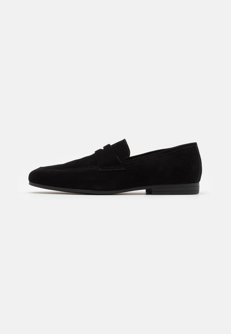 Mocassin pour homme en daim noir avec un petit talon et une bride sur le cou-de-pied, présenté de profil sur un fond blanc.