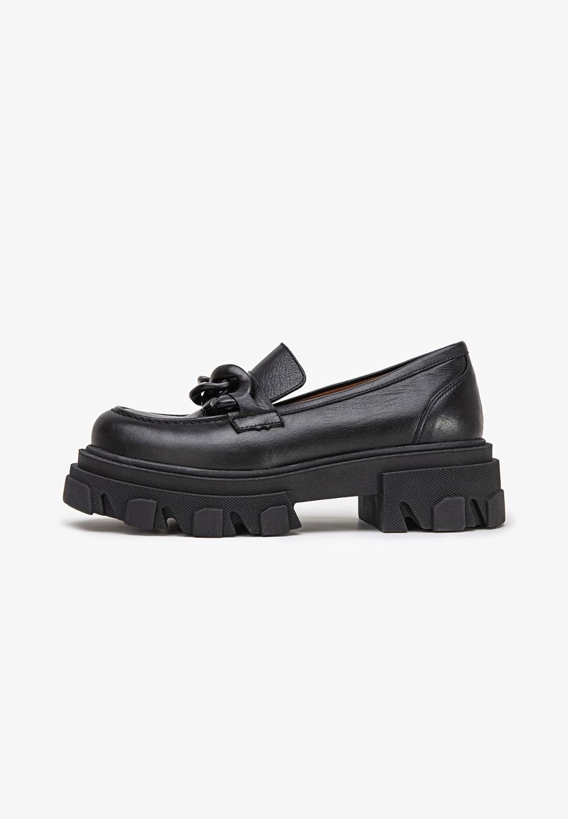 Mocassins en cuir noir avec une semelle épaisse et dentelée, ornés d'un nœud décoratif à l'avant. Texture lisse et design minimaliste.