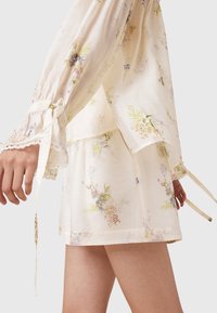 Floral printed dress in light beige fabric, featuring long sleeves, lace trim, and ties at the cuffs, with layered design and soft texture.