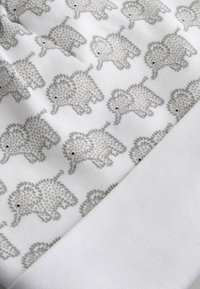 Puha fehér anyag, melyen kis, szürkés elefántok ismétlődő mintája látható, balra néznek, részben behajtva, hogy az alatta lévő sima fehér anyagot is megmutassa.