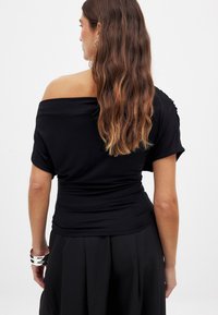 Must värvitu kaelusega ülemine osa, millel on pehme ja veniv kangas. Omab koondeid vöökohal ja lühikesi varrukaid, kantuna mustade seelikutega.