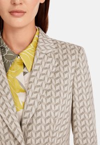Light gray blazer with a geometric pattern, paired with a yellow floral collared shirt. Smooth texture and structured fit.