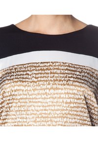 Top z krótkim rękawem z czarną górną częścią i dolną połową w złoty wzór z białymi abstrakcyjnymi wzorami. Gładka faktura.