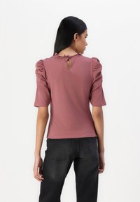 Kratke rokave, mauve top iz mehkega materiala z nabranimi rameni in ključavnico na hrbtu ter volančki na ovratniku.