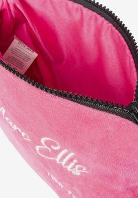 Tracolla in velluto rosa con cerniera nera. Interno foderato in tessuto rosa brillante. Presenta testo ricamato in bianco all'esterno.