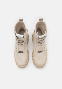 Paire de bottes montantes en daim beige avec semelles épaisses couleur tan et lacets, vues de dessus sur fond blanc.