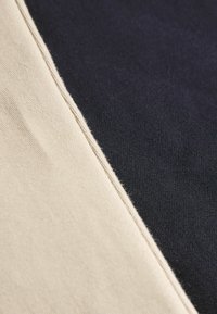 Sections en tissu crème et marine avec une texture lisse. Couture visible le long de la couture séparant les deux couleurs.