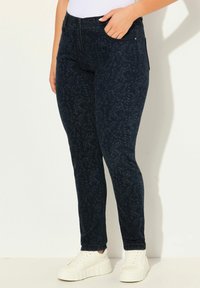 Mörkblå mönstrade jeans med ett bladdesign, slim fit, fyra fickor och resårmidja, i kombination med vita sneakers.