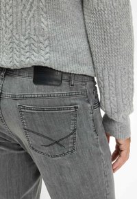 Grijze kabelgebreide trui met geribde manchetten, gecombineerd met donkergrijze jeans met een leren patch en geborduurd zakontwerp.