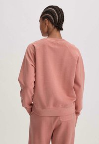 Felpa rosa con polsini e orlo a coste, presenta un colletto rotondo e maniche raglan. Tessuto morbido al tatto, vestibilità casual.