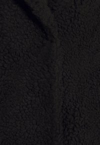 Tela de forro polar negra con una superficie suave y texturizada, que presenta un patrón peludo y mullido. El material parece grueso y cálido, adecuado para ropa exterior.