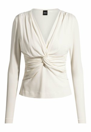 Long-sleeve women's top in cream, featuring a twisted front design, soft stretchy fabric, and a fitted silhouette with a scoop neckline.