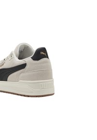 Baskets en daim gris clair avec un accent en cuir noir, dotées d'une semelle en caoutchouc et d'un logo doré sur le talon et sur le côté.