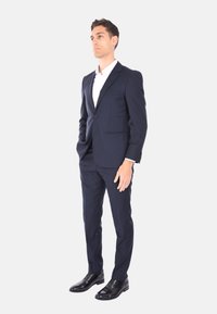 Completo blu navy realizzato in tessuto liscio, design aderente con chiusura a un bottone e taschino sul petto. Abbinato a scarpe in pelle nere.