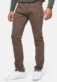Jeans de mezclilla marrones con un diseño ajustado, que cuentan con cinco bolsillos y detalles de costura sutiles. Combinados con zapatillas blancas para un contraste.