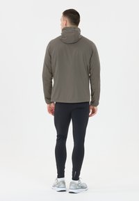 Vattentålig, huva, ljusgrå jacka med en jämn textur. Kombinerad med åtsittande svarta leggings och silverfärgade löparskor.