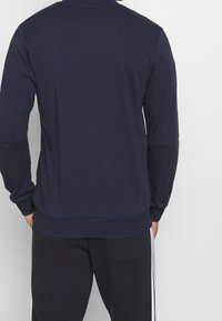 Felpa a girocollo navy con maniche lunghe, polsini e orlo a costine. Tessuto morbido, design minimalista, con etichetta laterale.
