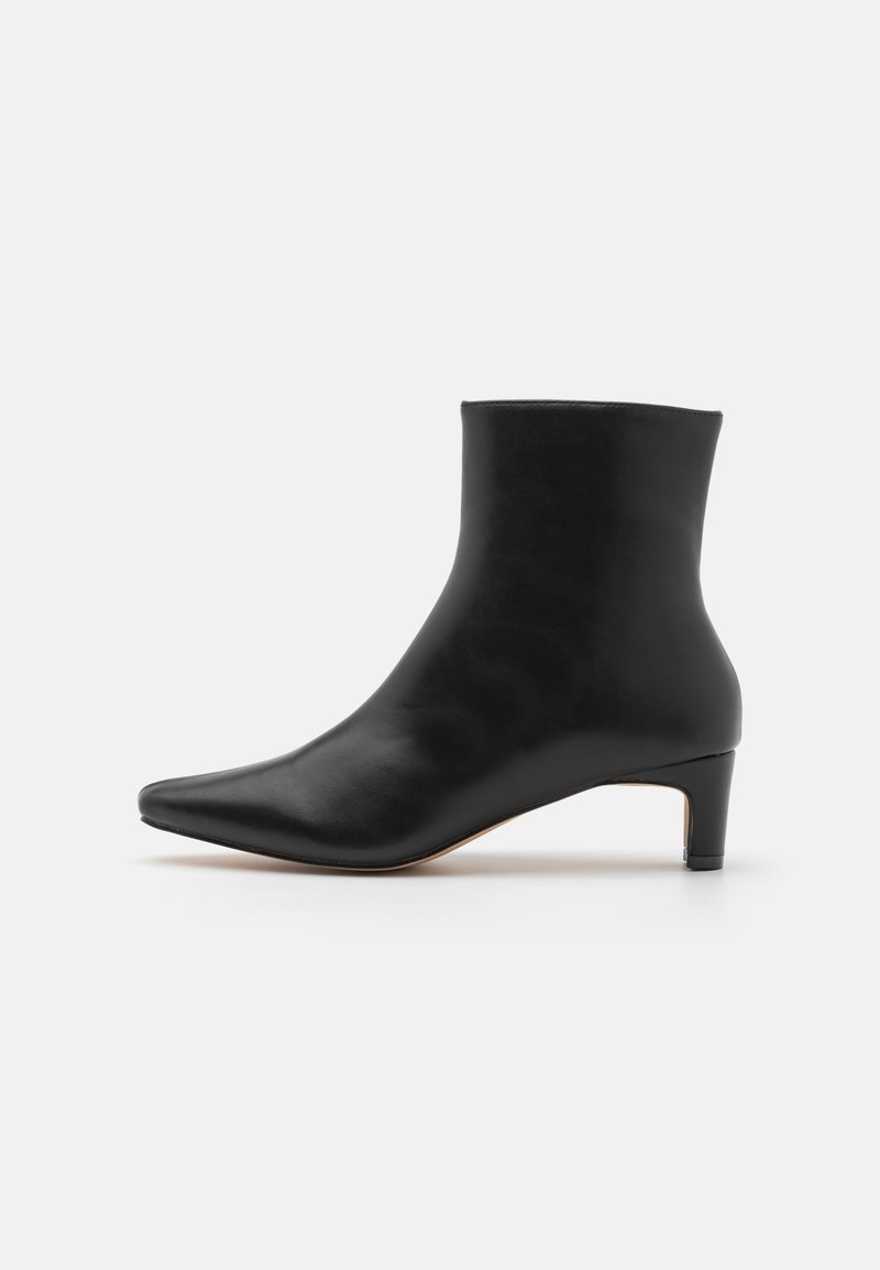 Bottine en cuir noir avec bout pointu et petit talon bas, sur fond blanc.
