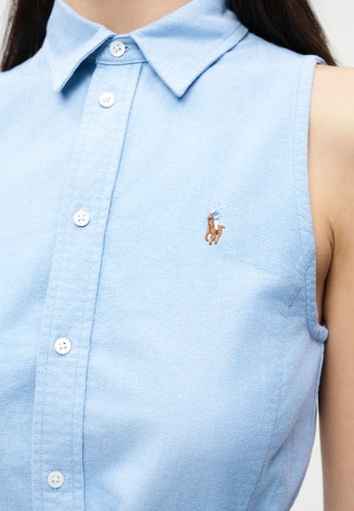 Gaiši zilas krāsas bezroku krekls ar apkakli un pogām, kreisajā krūtīs neliela izšūta polo spēlētāja logo.