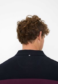 Marineblaues Poloshirt mit einem bordeauxroten Streifen, kurzem Kragen und strukturiertem Stoff. Zeigt ein kleines Logodetail auf der Rückseite des Kragens.