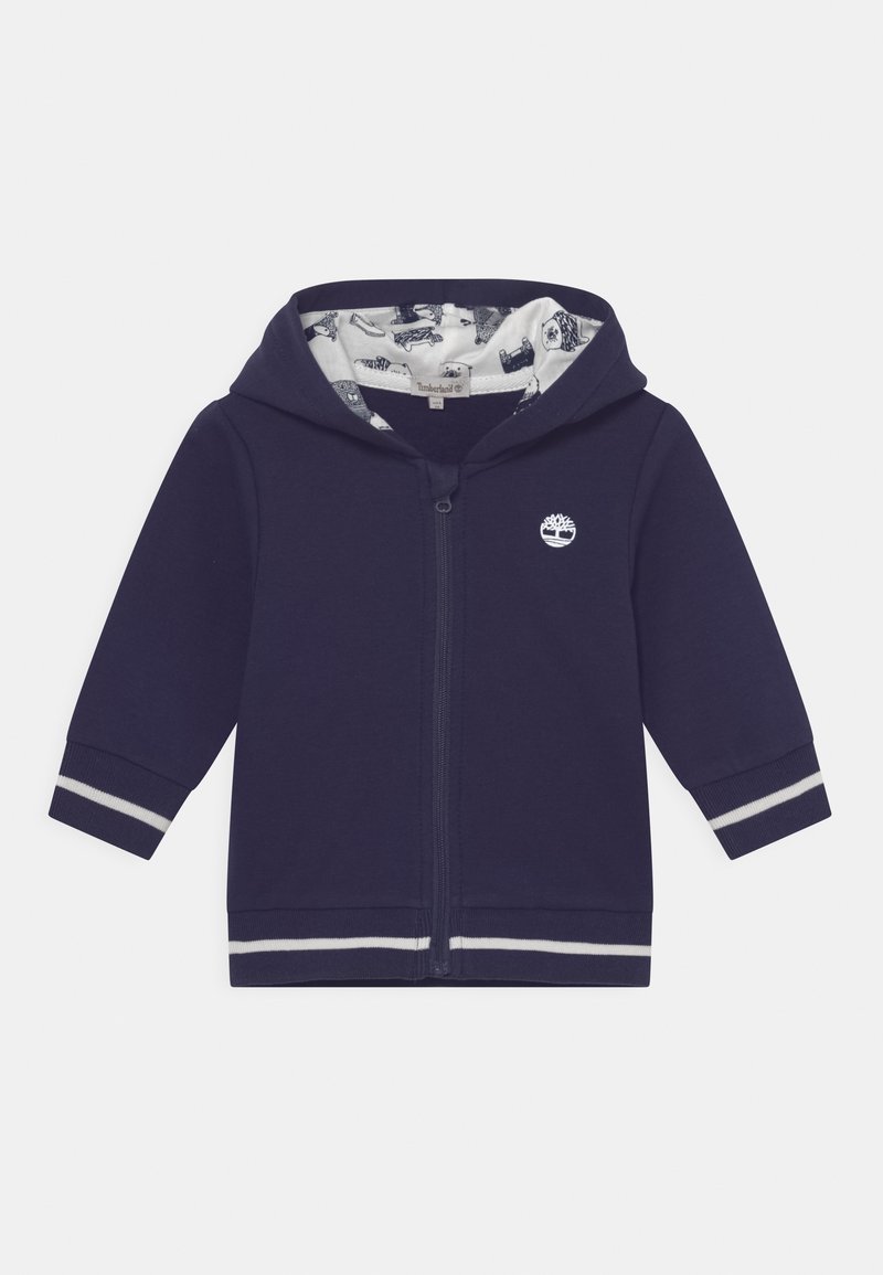 Felpa con zip blu navy con logo bianco, polsini a righe e fodera interna a motivi con varie illustrazioni grafiche.