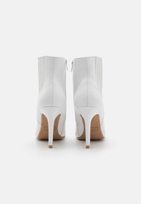 Bottines blanches à talons avec une finition en cuir lisse, des pointes effilées et des fermetures éclairs à l'arrière, présentant des détails de couture verticale sur les côtés.