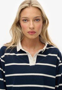 Navyblauw gestreept poloshirt met witte strepen en een contrasterende witte kraag; voorzien van drie knopen bij de kraag en een losse pasvorm.