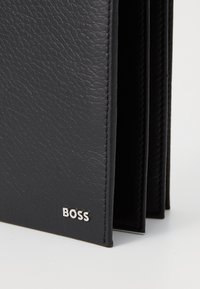 Čierna kožená peňaženka s textúrovaným povrchom, so strieborným logom "BOSS" a viditeľným prešívaním pozdĺž okrajov.