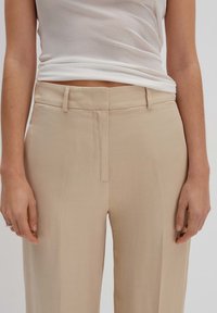 Beige skräddarsydda byxor med en slät yta, med rak benklippning, sidofickor och en diskret dragkedja fram.