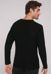 Schwarzes Langarmshirt mit geripptem Muster, rundem Ausschnitt und Seitenschlitzen, Rückansicht, figurbetontes Design.