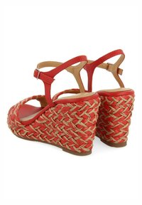 Sandalias rojas de cuña con un diseño de paja trenzada. Incluye un tacón trenzado texturizado, punta abierta y correa en el tobillo ajustable.