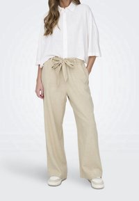 Lněné béžové kalhoty s širokým střihem a vázáním v pase, doplněné volnou bílou košilí na knoflíky. Hladký povrch, uvolněný střih a minimalistický design.