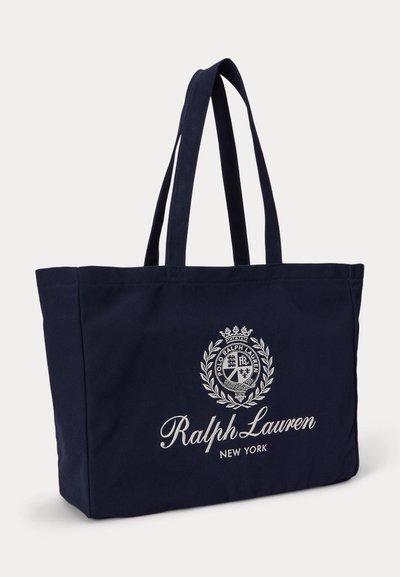 Τσάντα Ralph Lauren σε ναυτικό μπλε με διπλές λαβές και λευκό κεντημένο λογότυπο και έμβλημα στο μπροστινό μέρος, ελαφρώς στραμμένη προς τα δεξιά.