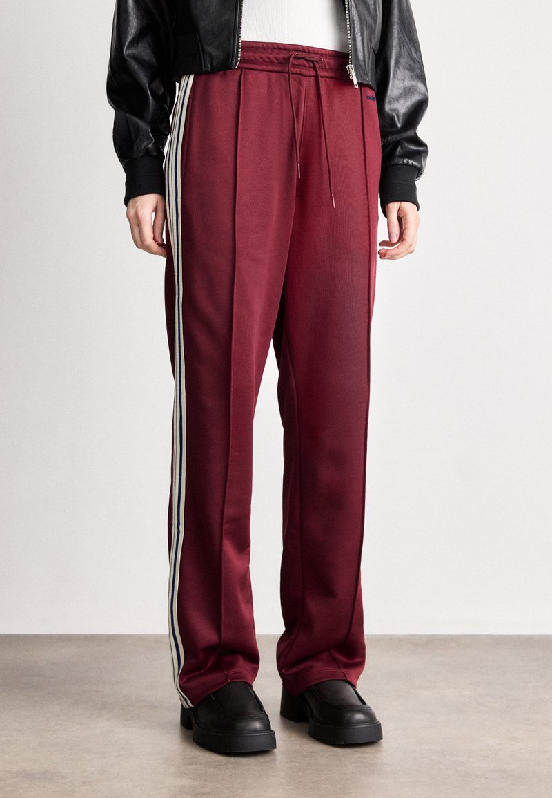 Μαρόν φόρμες σε μαλακό, υφασμάτινο υλικό με ρυθμιζόμενη μέση, με αντίθετες λευκές πλευρικές ρίγες και άνετη εφαρμογή. Μαύρα παπούτσια.