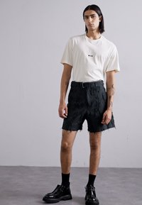 Hvit bomull t-skjorte med "MSGM"-logo, kombinert med svarte slitte shorts med frynser, iført svarte kraftige sko og sokker.