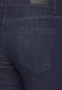 Tmavě modré džíny z denimu s klasickým pětikapsovým designem, úzkými nohavicemi a jemným stehovým vzorem na zadních kapsách.