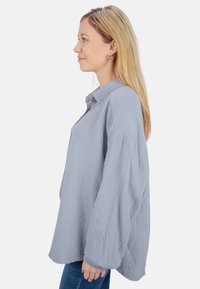 Light gray, oversized shirt made from textured fabric featuring a button-up collar and long, voluminous sleeves.