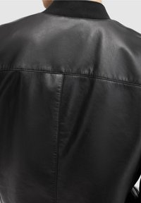 Svart läderjacka med en slät yta, ribbat krage och subtila sömdetaljer på ryggen. Enkel och klassisk design.