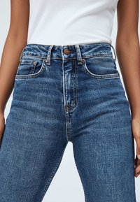 Jeans de denim azul de cintura alta con un diseño clásico, que cuentan con cinco bolsillos y costuras en contraste. Textura suave, tejido duradero.