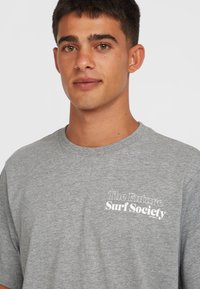 Šedé bavlněné tričko s kulatým výstřihem, krátkými rukávy a bílým potiskem "The Future Surf Society" na levé straně hrudníku.