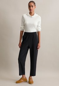 Haut à manches longues blanc côtelé avec capuche, assorti à un pantalon noir à taille élastique et des baskets jaune-brun avec des détails texturés.