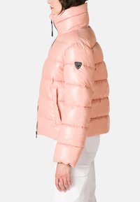 Giacca a vento rosa con collo alto, texture lucida, design trapuntato, tasche laterali e una patch del logo sulla manica sinistra.