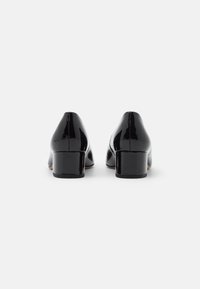 Černé lakované kožené lodičky na vysokém podpatku s kulatou špičkou, nízkým blokovým podpatkem a hladkým, odrazivým povrchem.