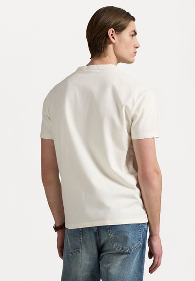 Camiseta de color crema de manga corta con cuello redondo clásico y diseño simple, combinada con unos jeans de mezclilla azul claro.